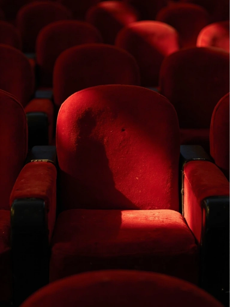 A single empty red velvet theater seat under a raking spotlight.